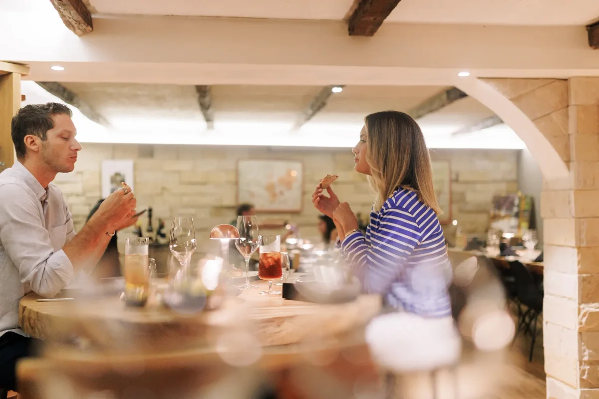 Un couple à table dans la cave du Carnotzet, entre les murs de pierre et les bouteilles