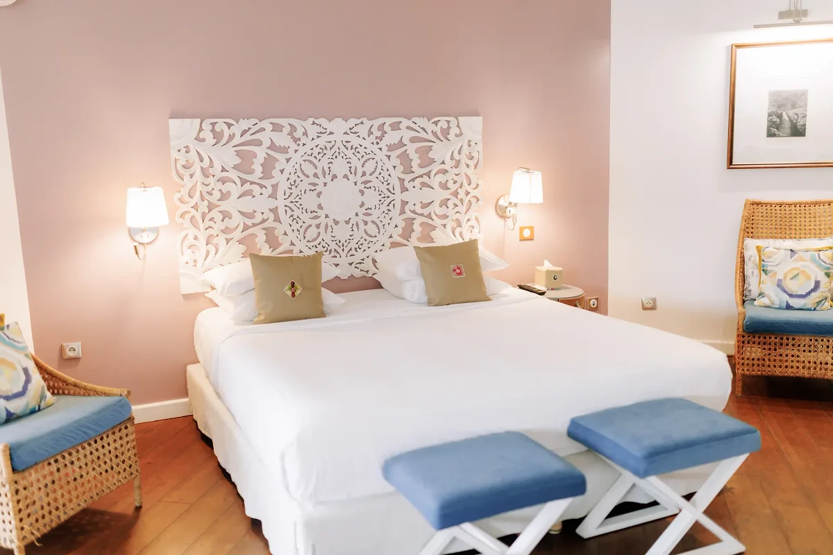 Une chambre double supérieure, son lit blanc et ses tabourets bleus